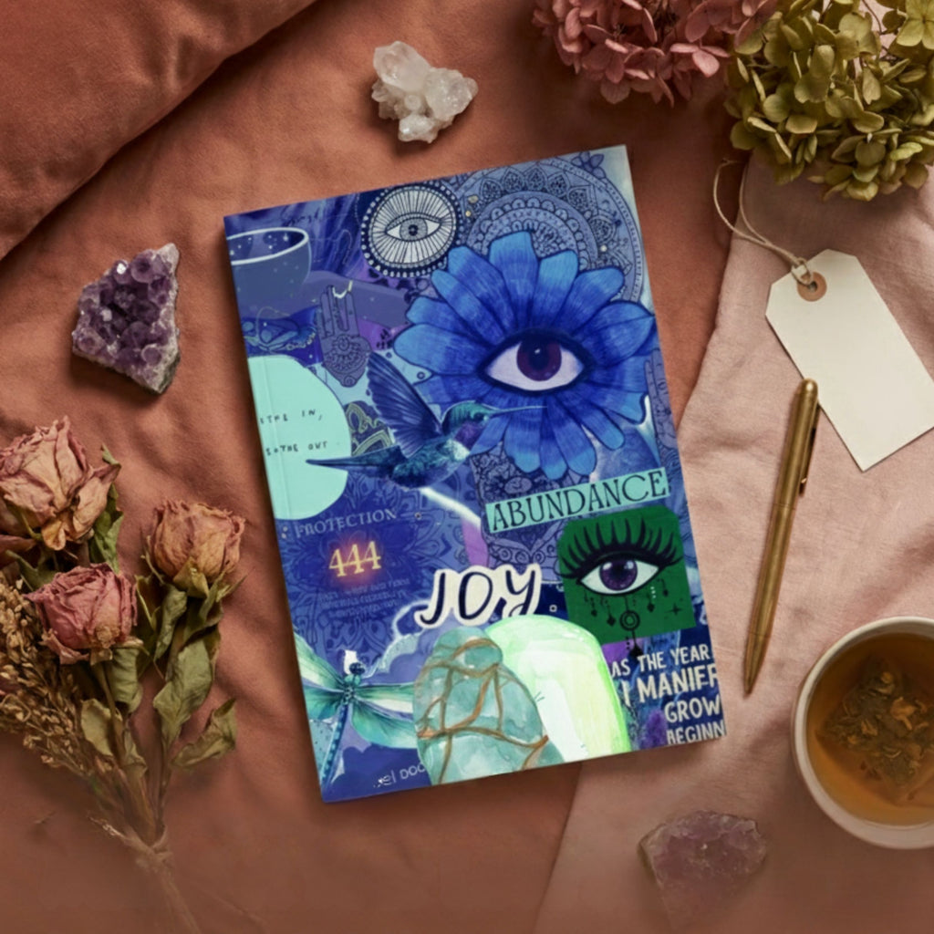 Joy abundance manifestation journal with illustrated cover, styled with candle, crystals, dried flowers and soft fabric background